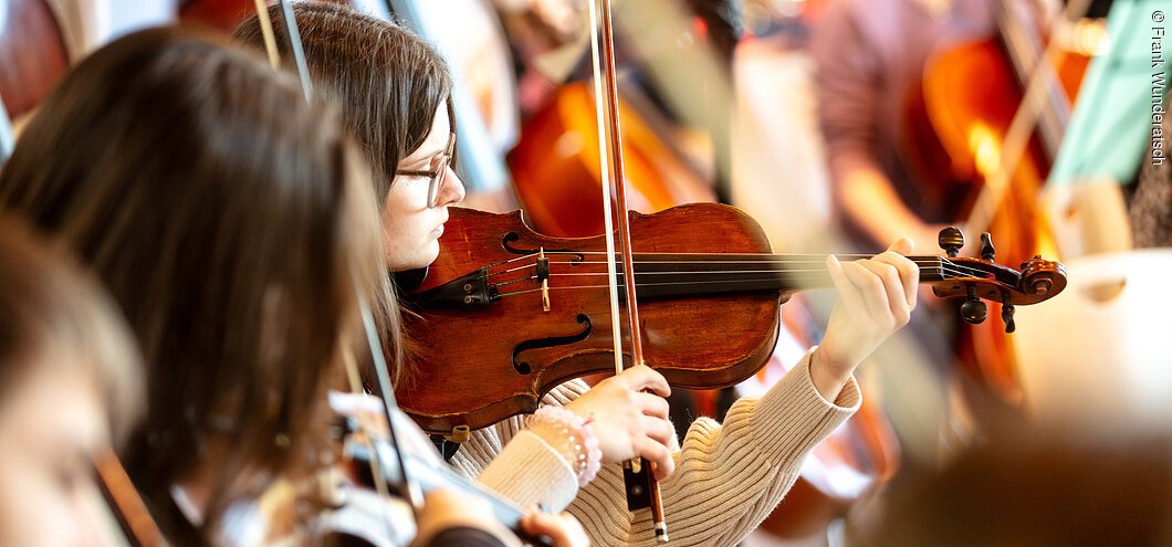 Eine junge Frau spielt Violine. Neben ihr ebenfalls eine Violinistin.